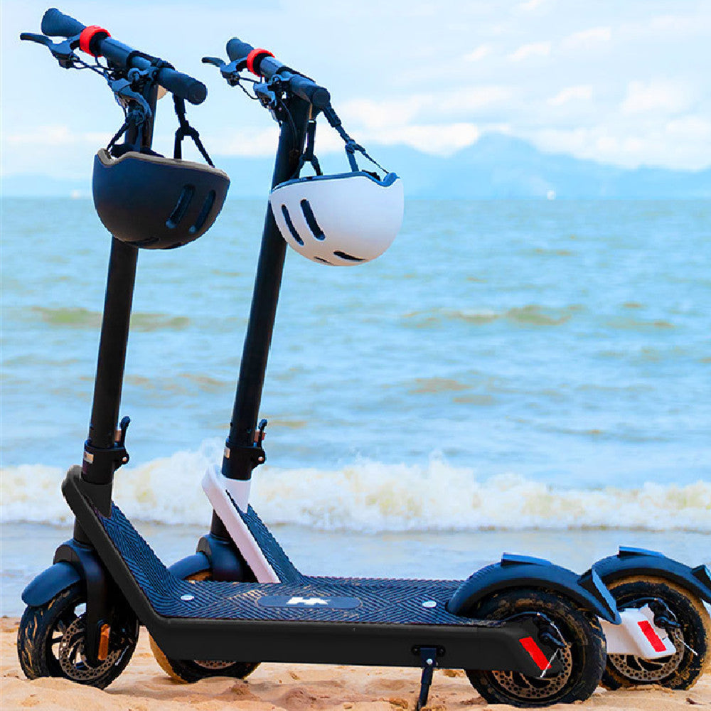 Two electric mobility scooters with helmets on a beach with ocean and sky in the background